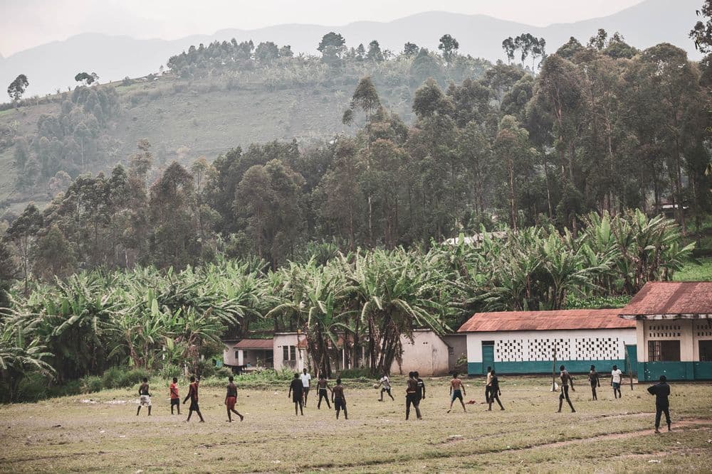 Youths playing football on a village field surrounded by hills and banana plantations