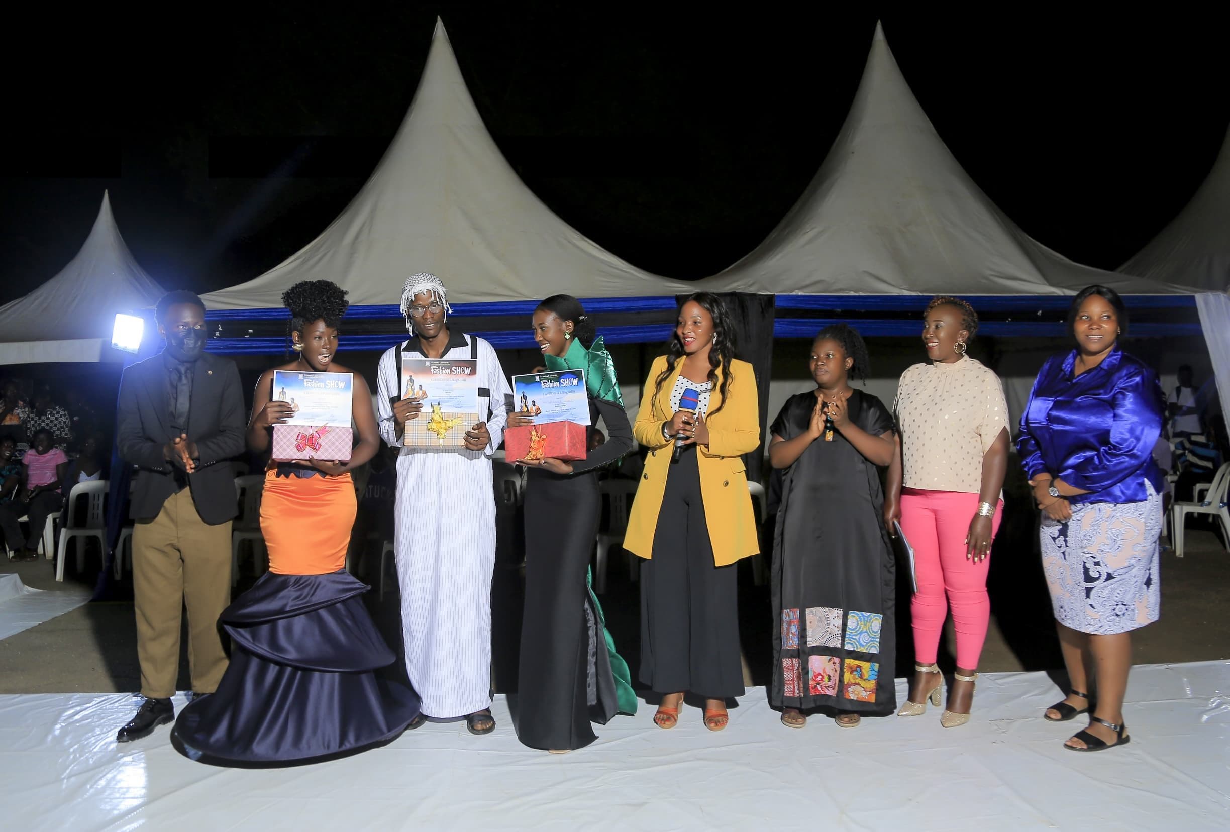 Recipients celebrating with certificates and gifts at an evening fashion show event